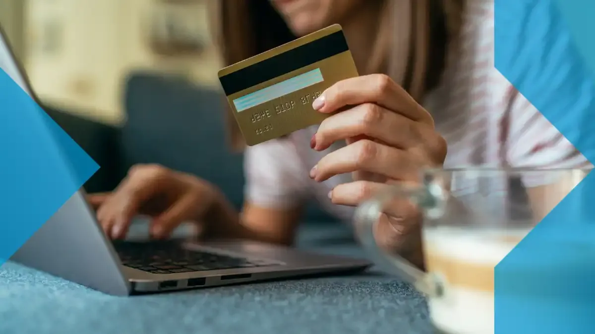 Pessoa segurando um cartão bancário enquanto usa um laptop, representando o lado digital dos pagamentos transfronteiriços e das transferências de dinheiro online.