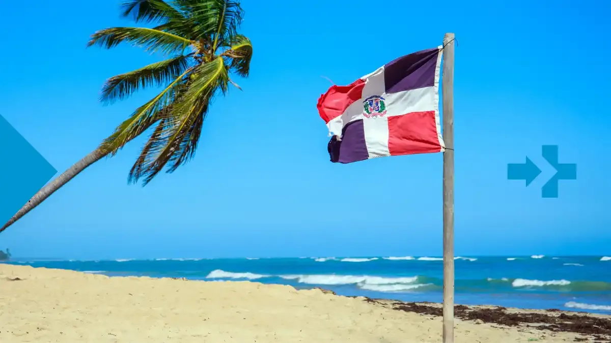 Dominican Republic flag waving on a tropical beach with a palm tree and blue sky.