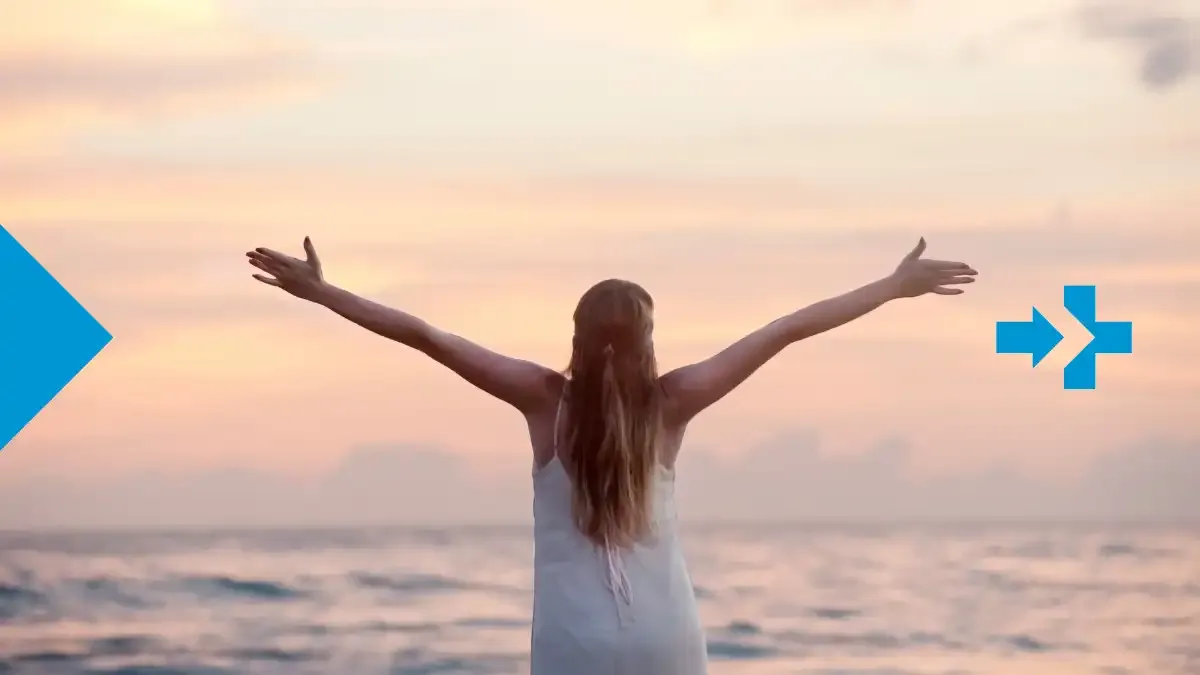 Woman facing the ocean with open arms at sunrise, symbolizing freedom and pride.