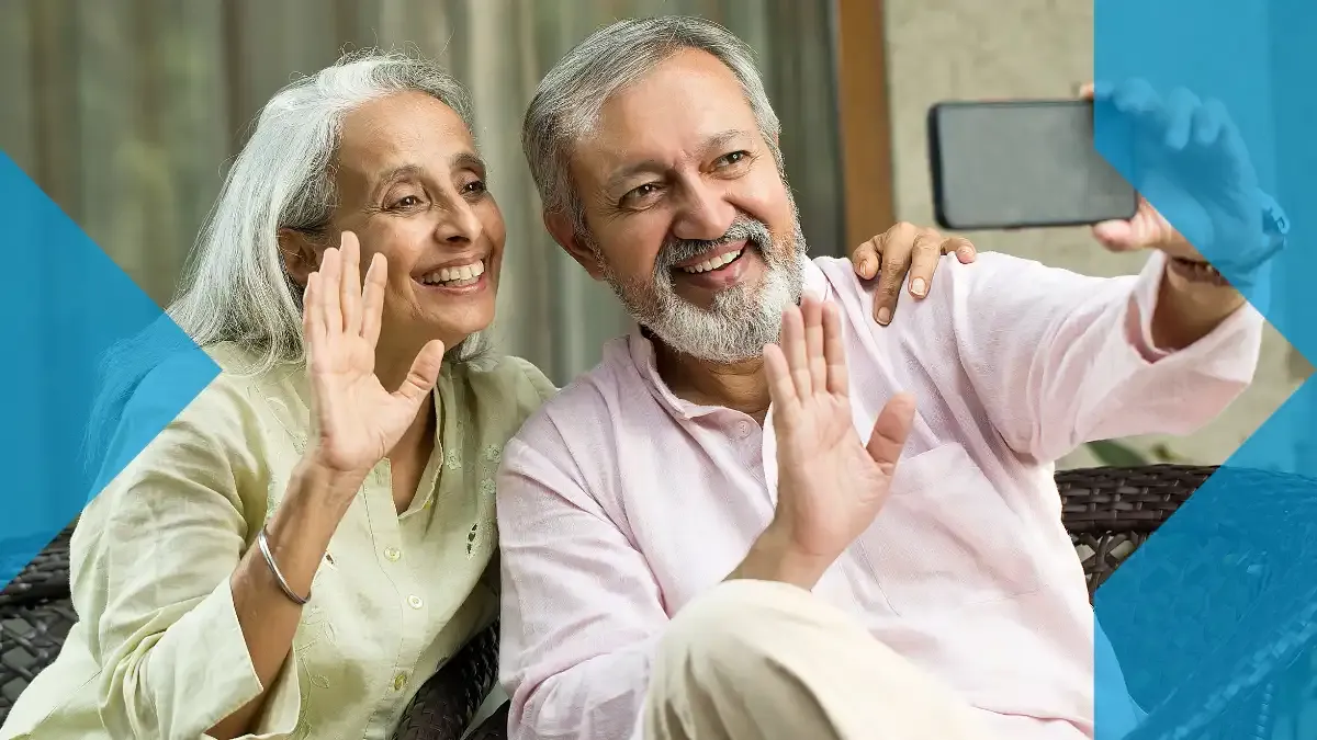 Casal idoso sorrindo e acenando em uma videochamada pelo smartphone, representando conexão à distância em 2026.