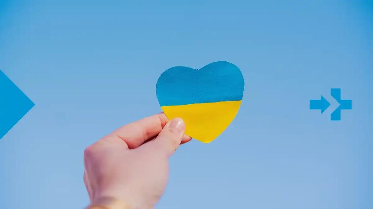 Hand holding a heart in the colors of the Ukrainian flag against a blue sky.