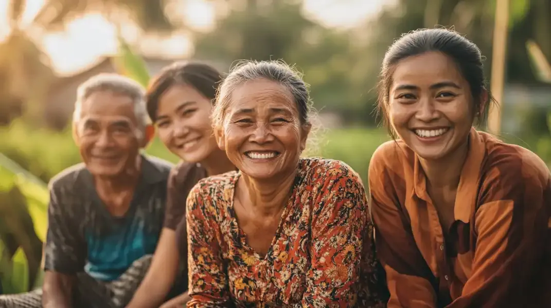Smiling multigenerational Indonesian family sitting together outdoors in a rural setting.
