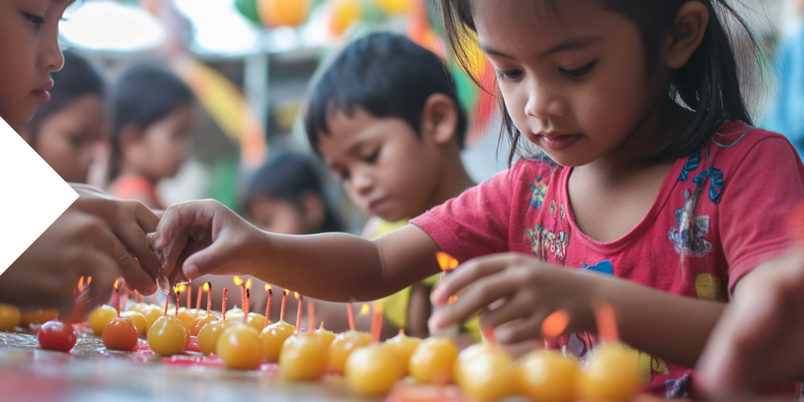 Young children carefully lighting small candles on a tray as part of a cultural celebration